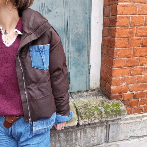 Doudoune marron à détails en jean, poche en jean sur le torse, finition en jean sur les poignets, et sur le bas de la doudoune.