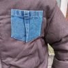 Doudoune marron à détails en jean, poche en jean sur le torse, finition en jean sur les poignets, et sur le bas de la doudoune.