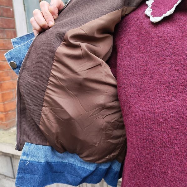 Doudoune marron à détails en jean, poche en jean sur le torse, finition en jean sur les poignets, et sur le bas de la doudoune.