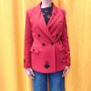 Blazer rouge épaules légèrement marquées. Motifs broderies noires (œil, cœur sacré, rouge à lèvres, diamant, revolver, rose, inscription " Ex-Wives Club). Tissu lisse et confortable, double rangée de boutons noires pour la fermeture, coupe ajustée.