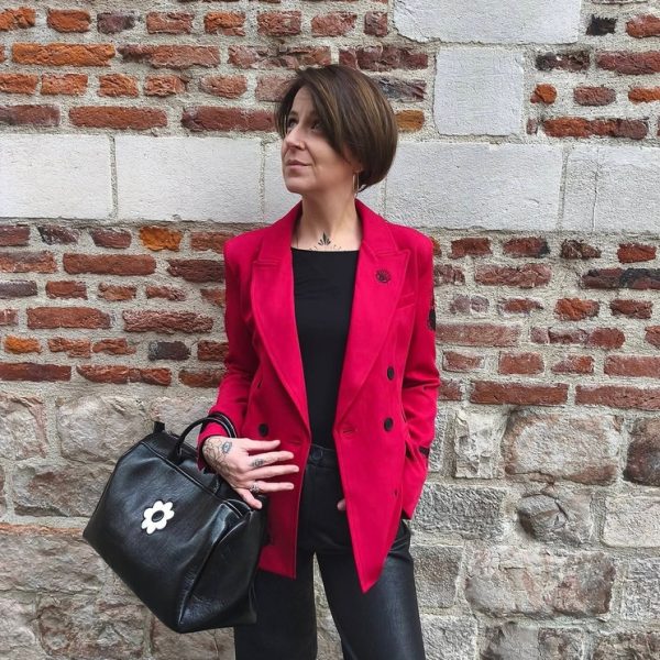 Blazer rouge épaules légèrement marquées. Motifs broderies noires (œil, cœur sacré, rouge à lèvres, diamant, revolver, rose, inscription " Ex-Wives Club). Tissu lisse et confortable, double rangée de boutons noires pour la fermeture, coupe ajustée.
