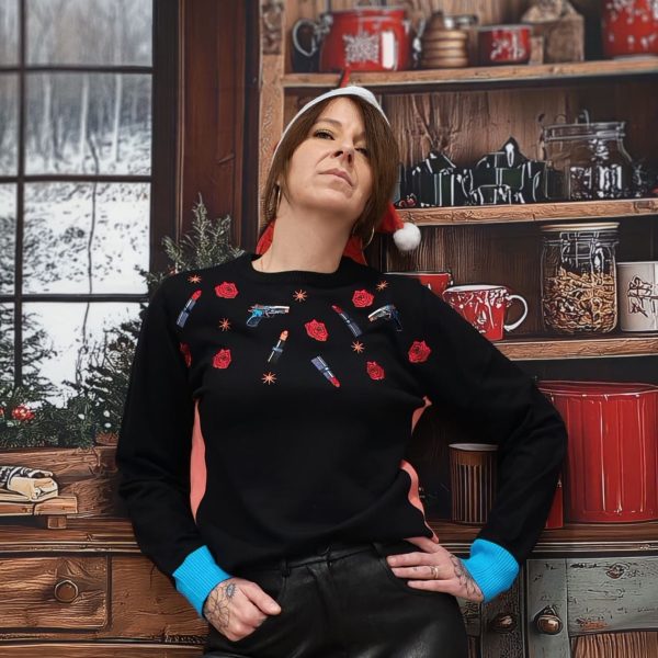 Pull "Guns & Glam" de couleur noir. Motifs brodés et imprimés : roses, rouges à lèvres, icônes pop art, bords-côtes contrastés, rose poudré à la taille, bleu vif aux poignets. Coupe féminine légèrement ajustée, maille douce et agréable.