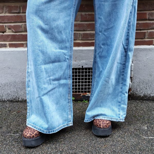 Jeans large taille haute denim bleu clair fermeture avec une patte de boutonnage croisé qui crée un effet asymétrique à la taille.