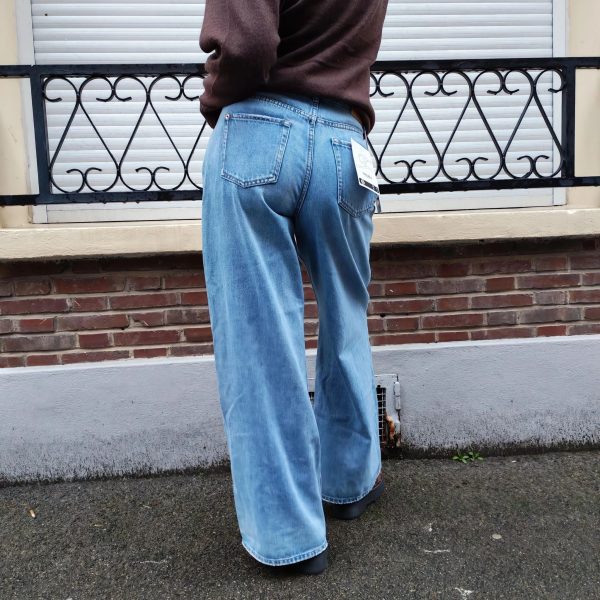 Jeans large taille haute denim bleu clair fermeture avec une patte de boutonnage croisé qui crée un effet asymétrique à la taille.