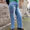 Jean barrel brodé love Jeans Mademoiselle Hélène Jean barrel brodé love, taille haute, denim clair délavé, broderies cœurs, fleurs et inscription, fermeture bouton + zip, longueur cheville / pleine longueur selon taille.