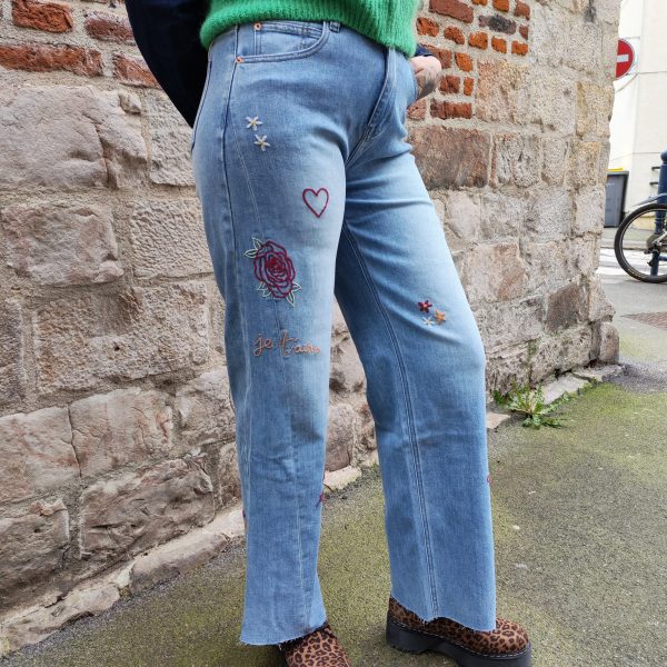Jean barrel brodé love Jeans Mademoiselle Hélène Jean barrel brodé love, taille haute, denim clair délavé, broderies cœurs, fleurs et inscription, fermeture bouton + zip, longueur cheville / pleine longueur selon taille.