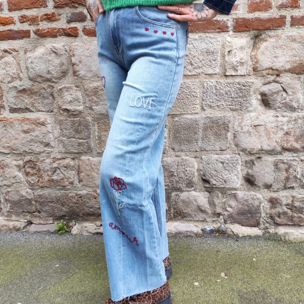 Jean barrel brodé love Jeans Mademoiselle Hélène Jean barrel brodé love, taille haute, denim clair délavé, broderies cœurs, fleurs et inscription, fermeture bouton + zip, longueur cheville / pleine longueur selon taille.