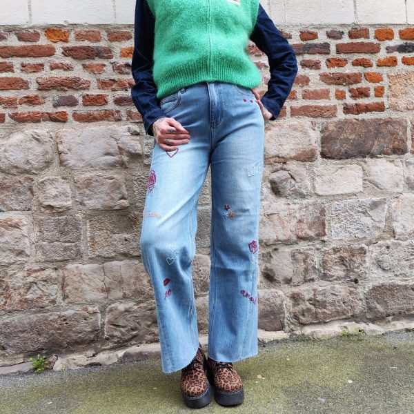 Jean barrel brodé love Jeans Mademoiselle Hélène Jean barrel brodé love, taille haute, denim clair délavé, broderies cœurs, fleurs et inscription, fermeture bouton + zip, longueur cheville / pleine longueur selon taille.
