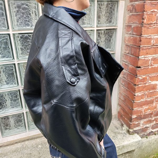 Veste simili cuir noire structurée, effet cuir texturé, coupe oversize, col montant avec boutons, fermeture zip frontal avec rabat asymétrique. Taille unique