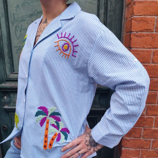 Chemise rayée brodée tropical Dernières Chances Mademoiselle Hélène Chemise rayée brodée tropicale, rayures verticales, broderies multicolores motif tropical, coupe confortable, légèrement ample, fermeture boutonnée sur le devant, col chemise classique, manches longues avec poignets boutonnés, matière légère et agréable à porter.