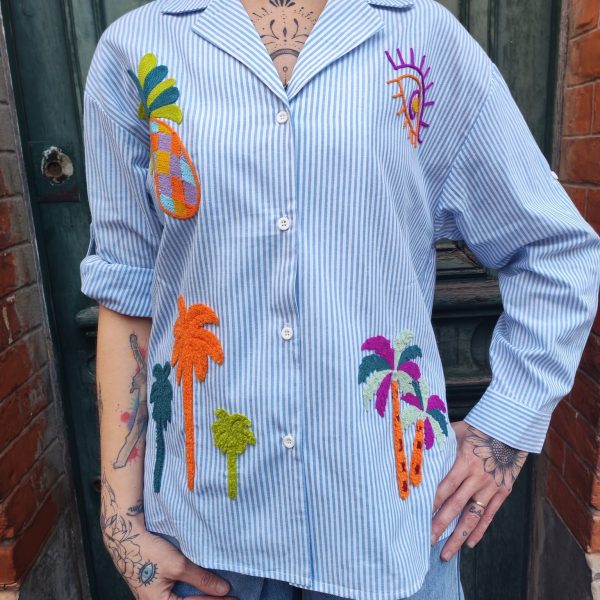 Chemise rayée brodée tropical Dernières Chances Mademoiselle Hélène Chemise rayée brodée tropicale, rayures verticales, broderies multicolores motif tropical, coupe confortable, légèrement ample, fermeture boutonnée sur le devant, col chemise classique, manches longues avec poignets boutonnés, matière légère et agréable à porter.