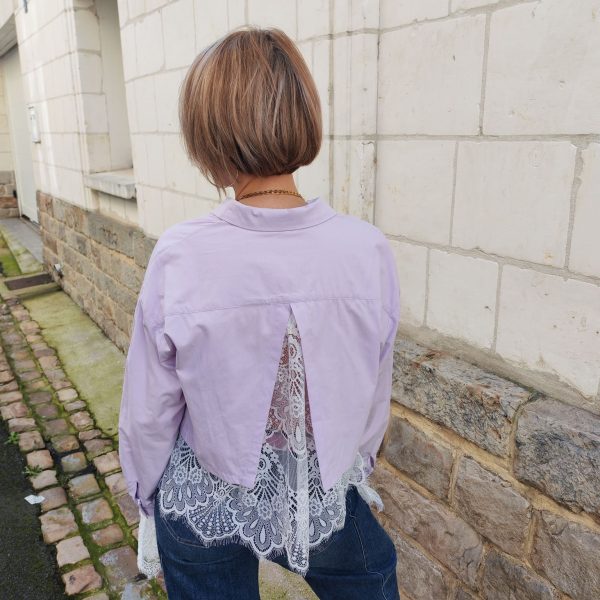 Chemise courte dentelle lilas, courte et légèrement ample, manches longues finitions dentelle, fermeture boutonnée sur le devant.