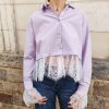 Chemise courte dentelle lilas, courte et légèrement ample, manches longues finitions dentelle, fermeture boutonnée sur le devant.