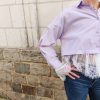 Chemise courte dentelle lilas, courte et légèrement ample, manches longues finitions dentelle, fermeture boutonnée sur le devant.