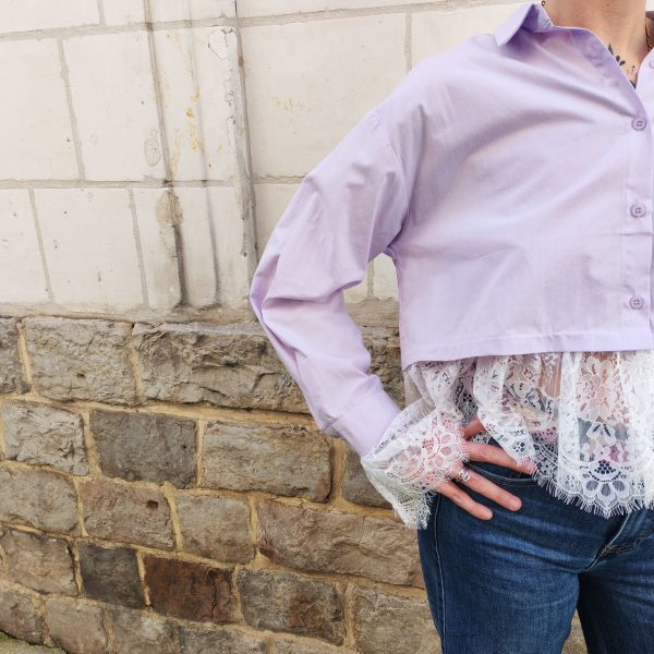 Chemise courte dentelle lilas, courte et légèrement ample, manches longues finitions dentelle, fermeture boutonnée sur le devant.