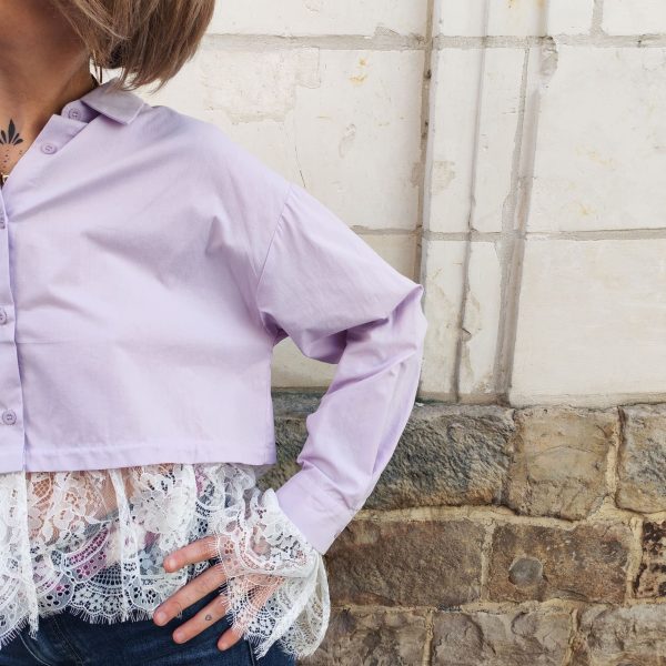 Chemise courte dentelle lilas, courte et légèrement ample, manches longues finitions dentelle, fermeture boutonnée sur le devant.
