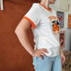 T-shirt orange brodé vintage Les hauts Mademoiselle Hélène T-shirt orange brodé vintage. T-shirt blanc avec détails orange contrastants Broderie orange et noire sur le devant Inscription "ORANGE - Pour Rome Italy" Manches courtes Col rond contrasté Coupe confortable Style rétro / vintage Matière douce et agréable à porter Taille normalement Facile à associer au quotidien Disponible en boutique et en ligne Livraison gratuite en France et en Belgique Retrait possible en boutique Les Curiosités Composition : 100% coton